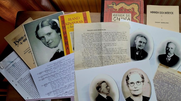 A collection of historical documents and books, including old photographs of individuals, letters, and titles in Swedish, on a wooden table.